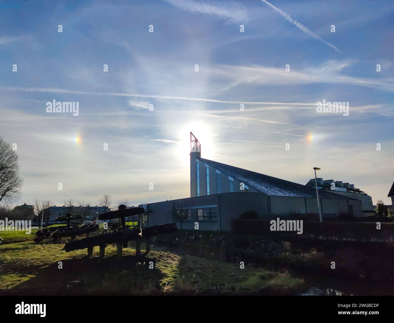 Sundogs or mocksuns on either side of the sun which is just behind the spire of a church. Stock Photo