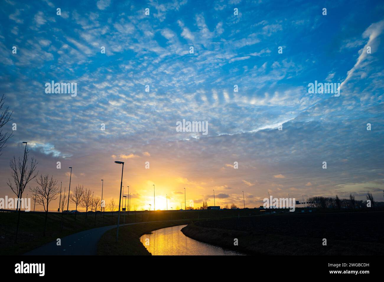 Evening sky with altocumulus wave clouds as the sun sets over the Dutch landscape. Stock Photo