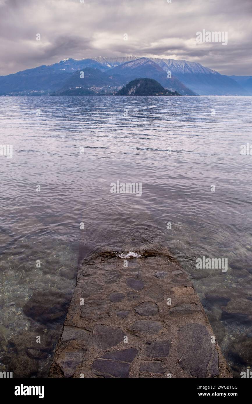 Stone walkway into lake with mountain backdrop in winter, Varenna, Lake