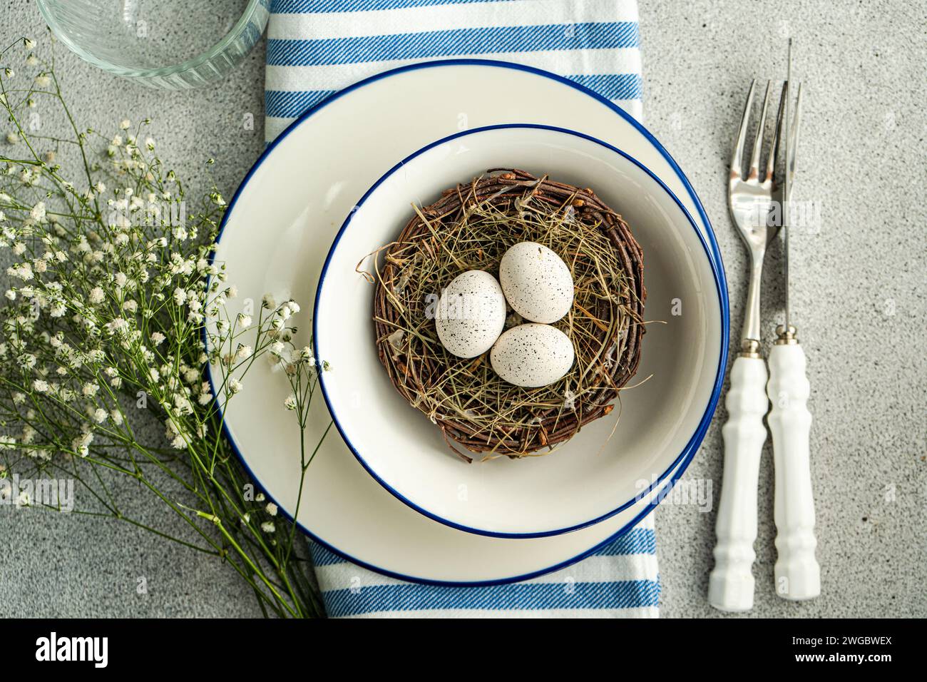 Overhead view of an Easter place setting with  white gypsophila flowers and a bird's nest with painted Easter eggs and feathers Stock Photo