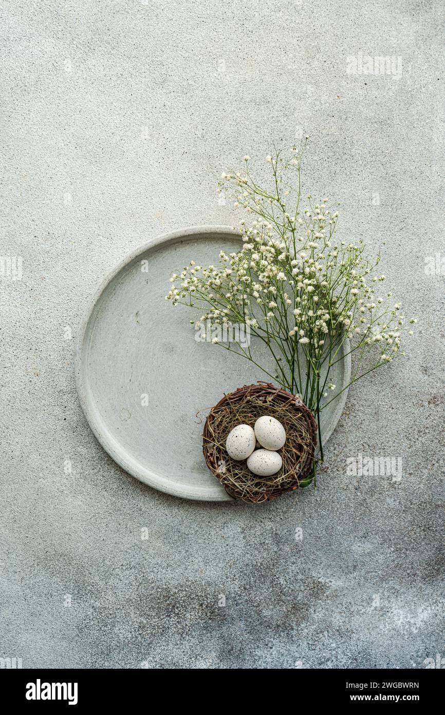 Overhead view of white gypsophila flowers and a bird's nest with Easter eggs on a ceramic plate Stock Photo