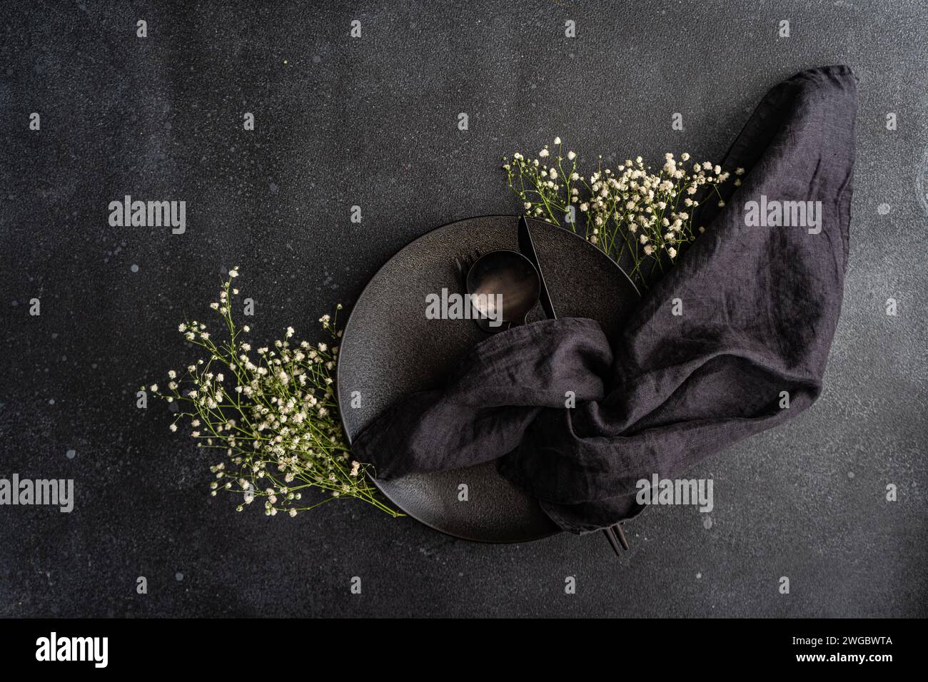 Overhead view of a black place setting with white gypsophila flowers on a black background Stock Photo