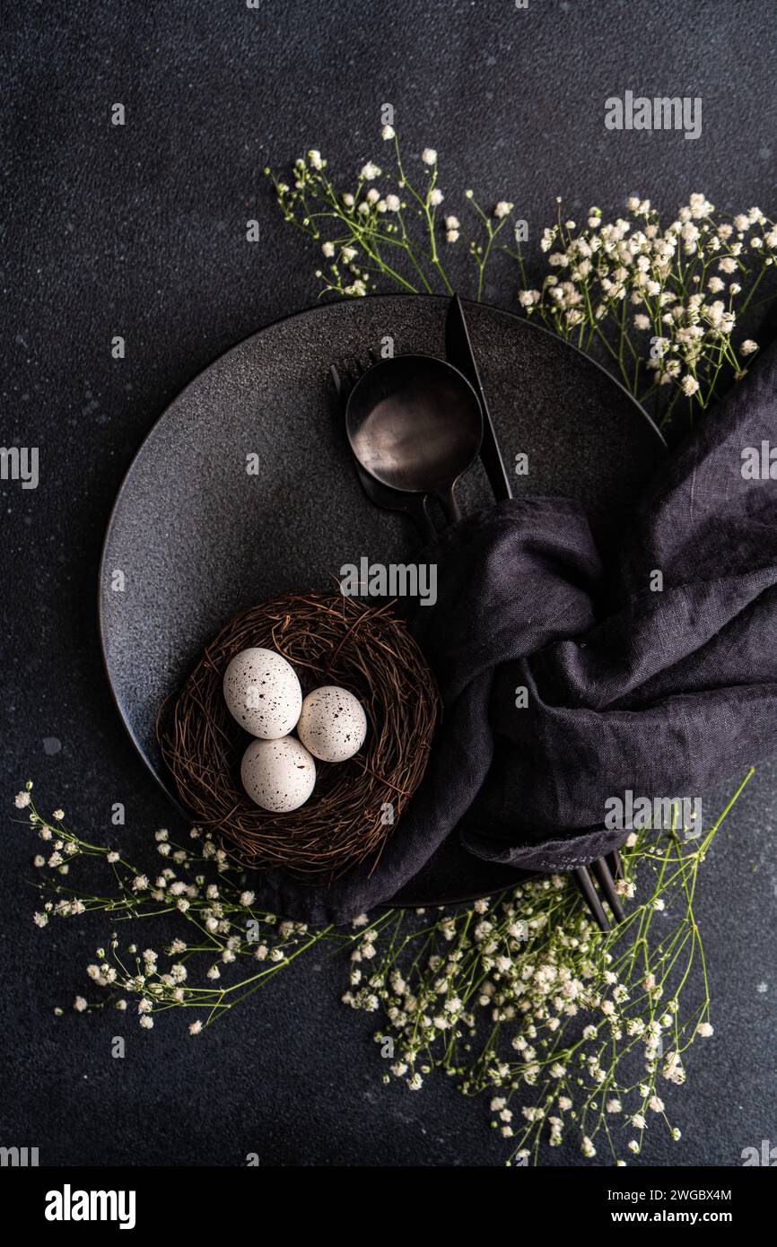 Overhead view of a black place setting with white gypsophila flowers and a bird's nest with Easter eggs on a black background Stock Photo