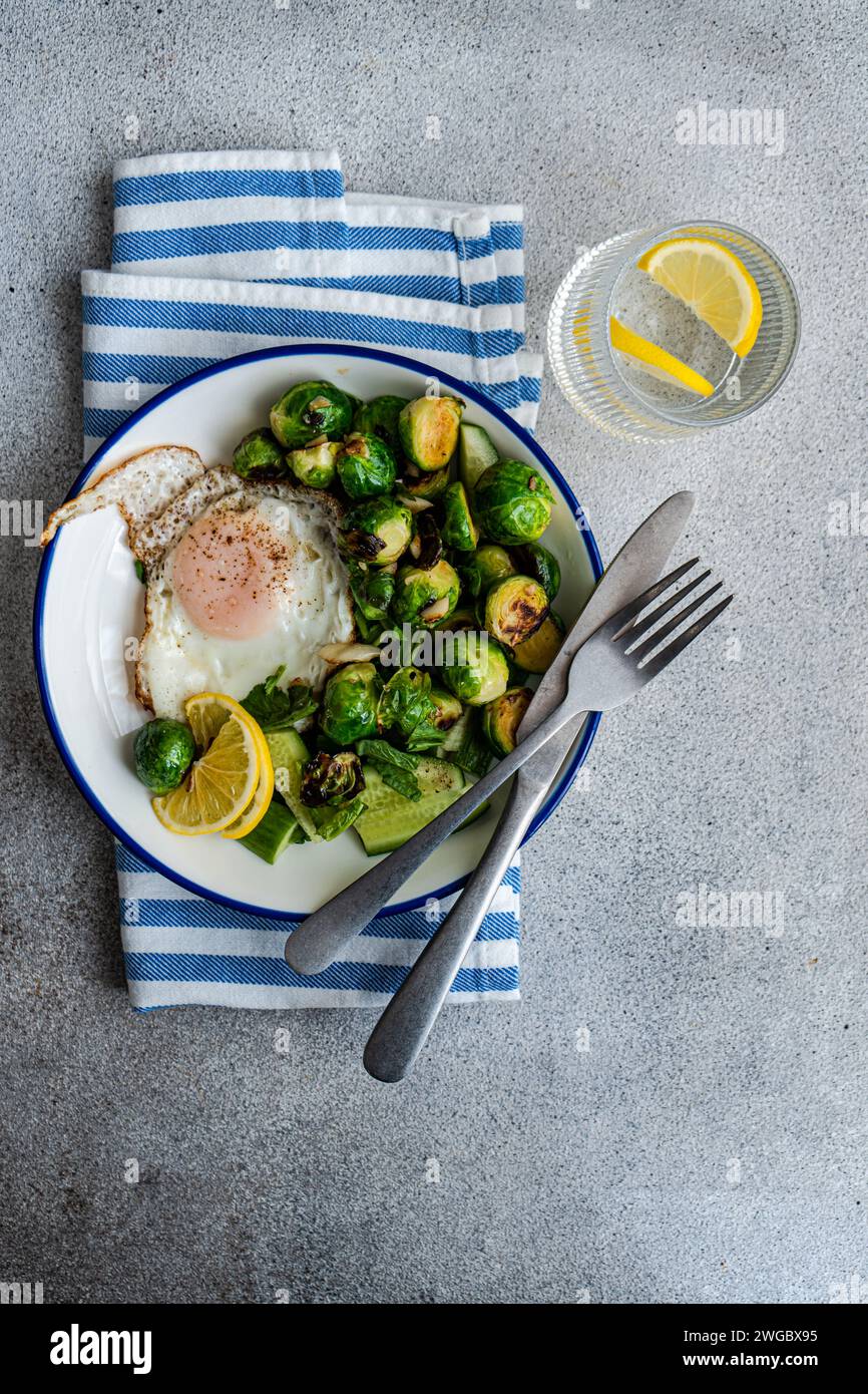 Overhead view of a fried egg with grilled Brussels sprouts, cucumber salad and a glass of lemon water Stock Photo