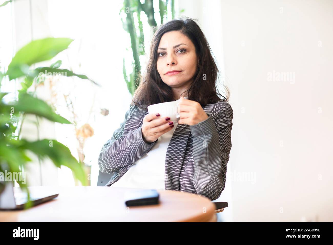 Businesswoman sitting in an office drinking a cup of coffee Stock Photo