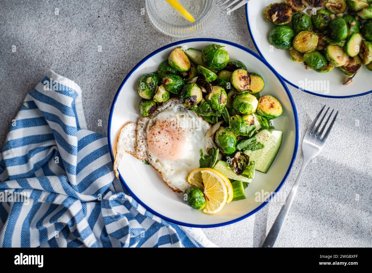 Overhead view of a fried egg with grilled Brussels sprouts, cucumber salad and a glass of lemon water Stock Photo