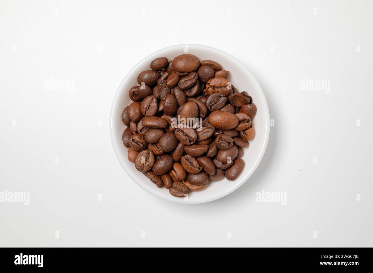, Food, 04.02.2024,  Minimalistische Komposition einer weißen Schüssel gefüllt mit gerösteten Kaffeebohnen, die auf einem hellen Untergrund steht, per Stock Photo