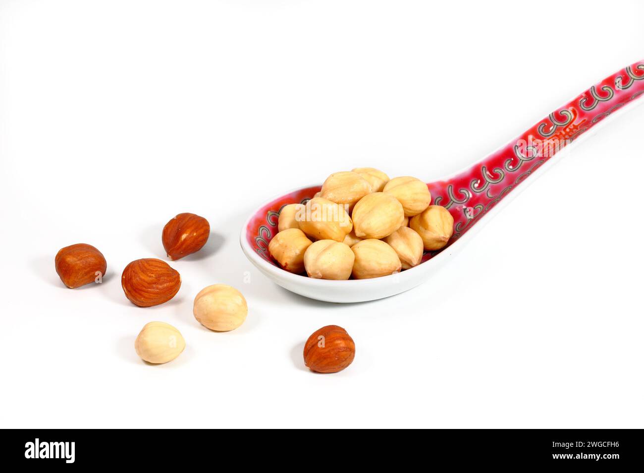 A soup spoon of shelled, dry toasted Oregon hazelnuts, Corylus americana, 榛果, some peeled, some unpeeled isolated on a white background. Stock Photo