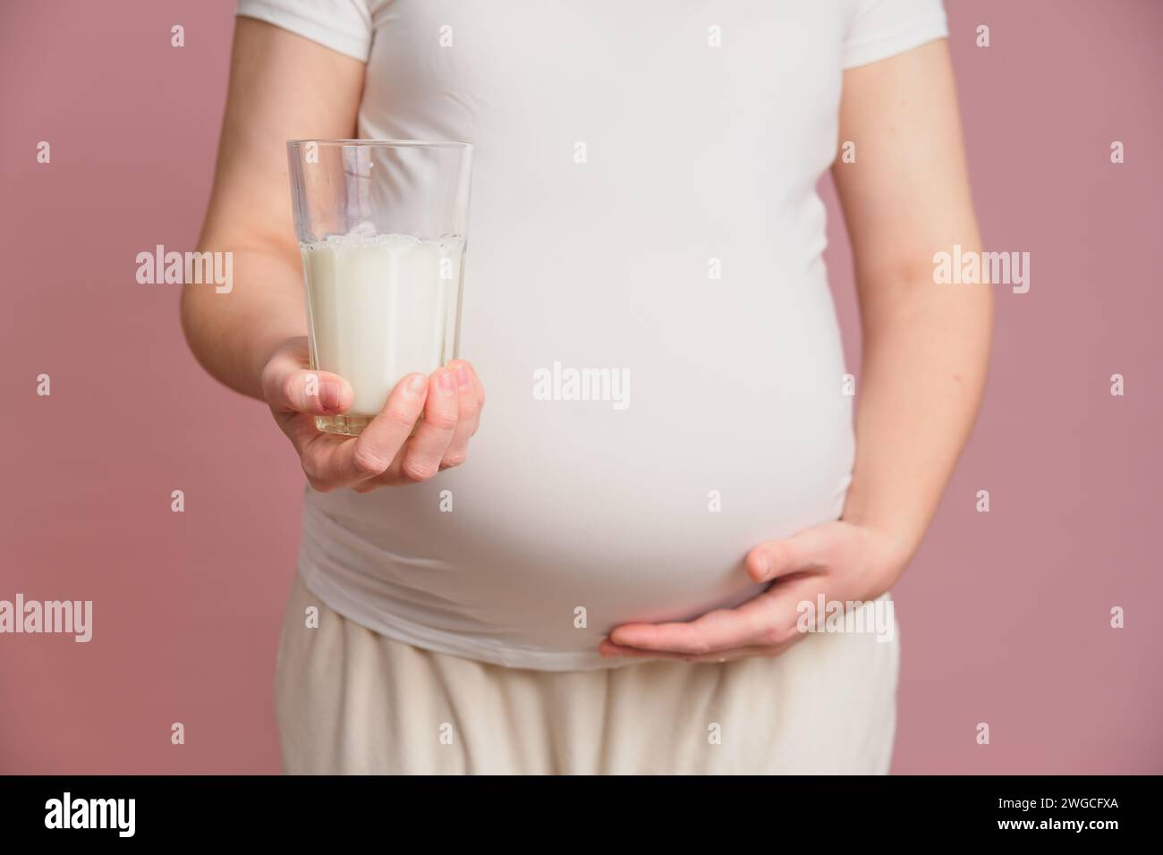 Pregnant woman holding a glass of milk in her hand, studio pink background. Concept of pregnancy and proper nutrition Stock Photo