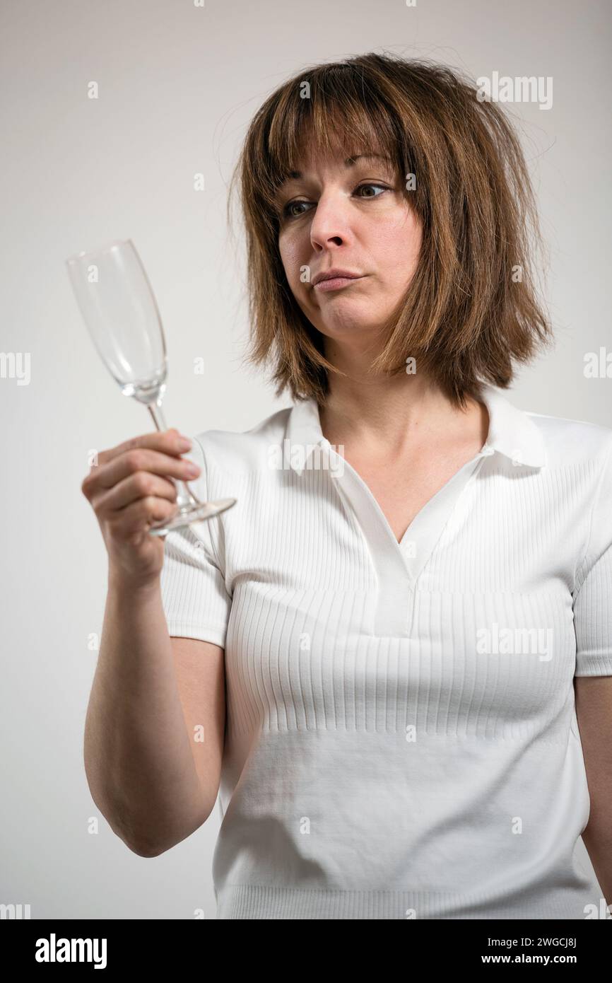 Caucasian woman looking at empty champagne glass, white background. Conceptual image of The Dry Challenge. Stock Photo