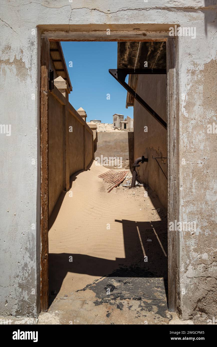 An aged entrance revealing a sandy path amid structures in a desert town Stock Photo