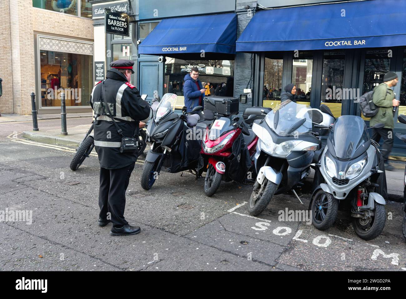 A parking attendant issuing a penalty notice parking ticket to motor bikes parked outside a marked designated area in the city of London England UK Stock Photo