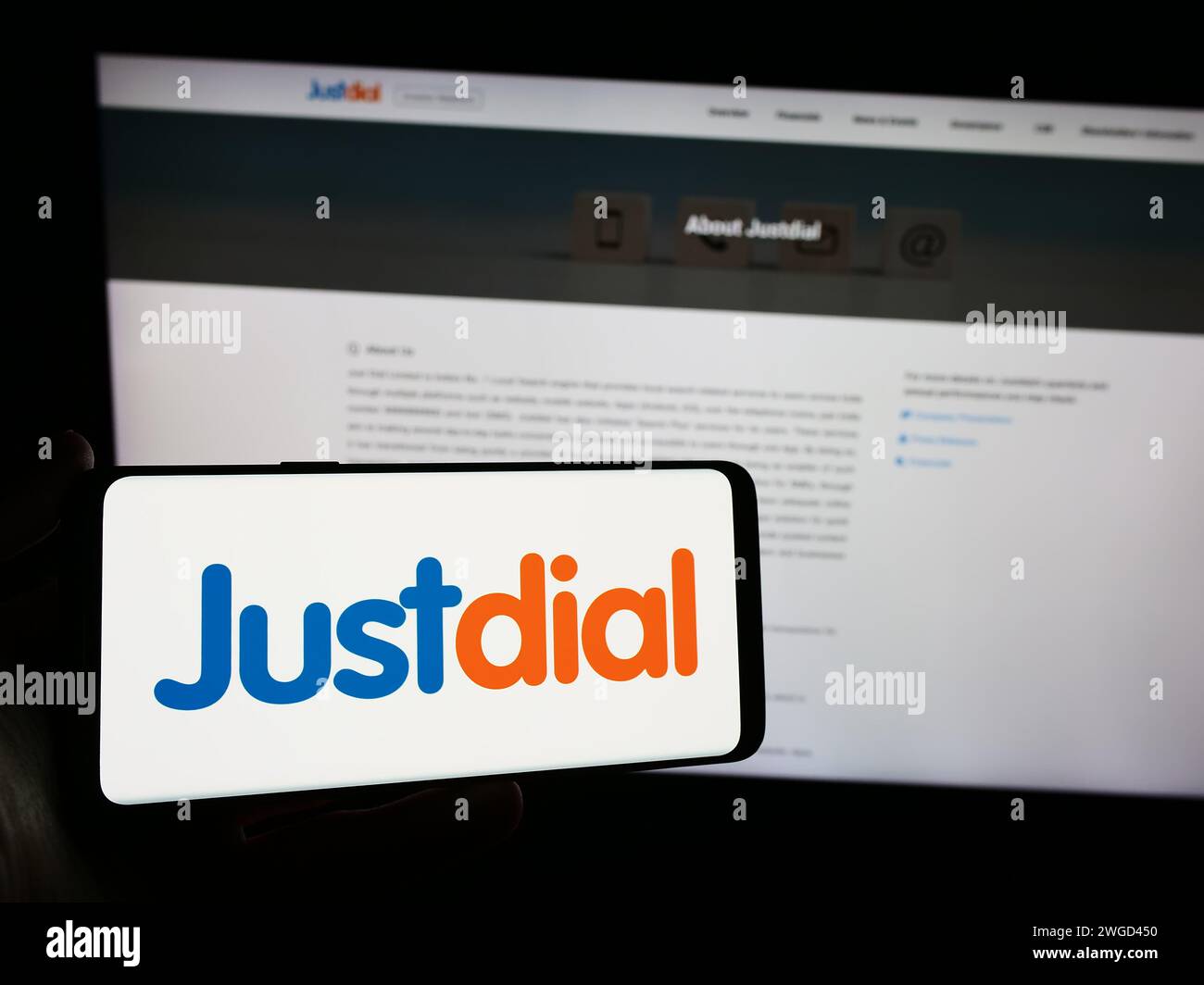 Person holding mobile phone with logo of Indian technology company Just Dial Limited (Justdial) in front of web page. Focus on phone display. Stock Photo