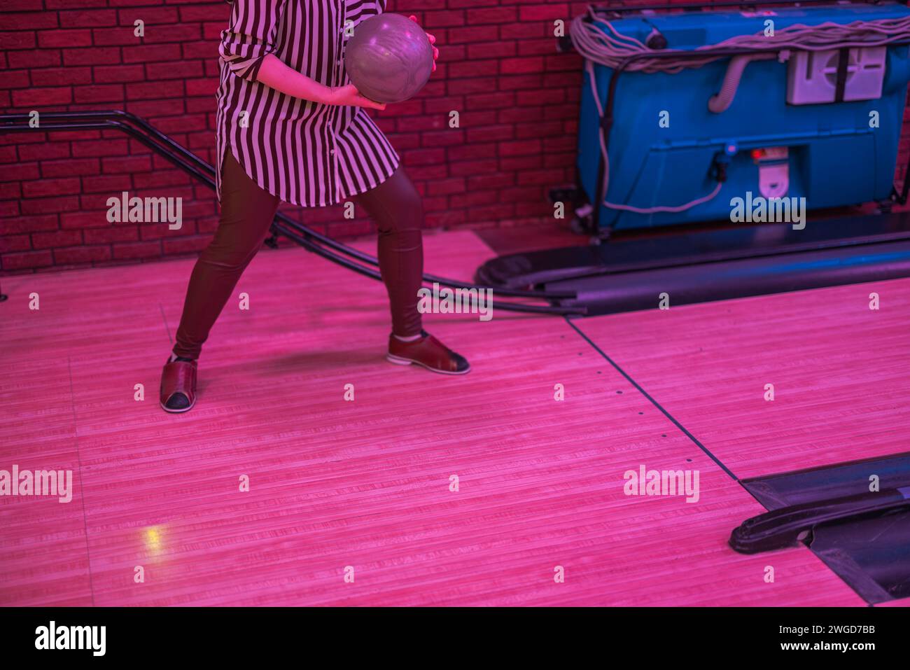View of a girl throwing a ball down the bowling lane to knock down pins