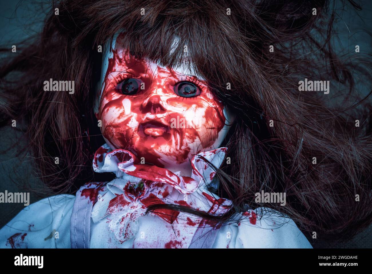 Possessed creepy horror doll with blood smeared all over her face in a cold dark moody tone Stock Photo
