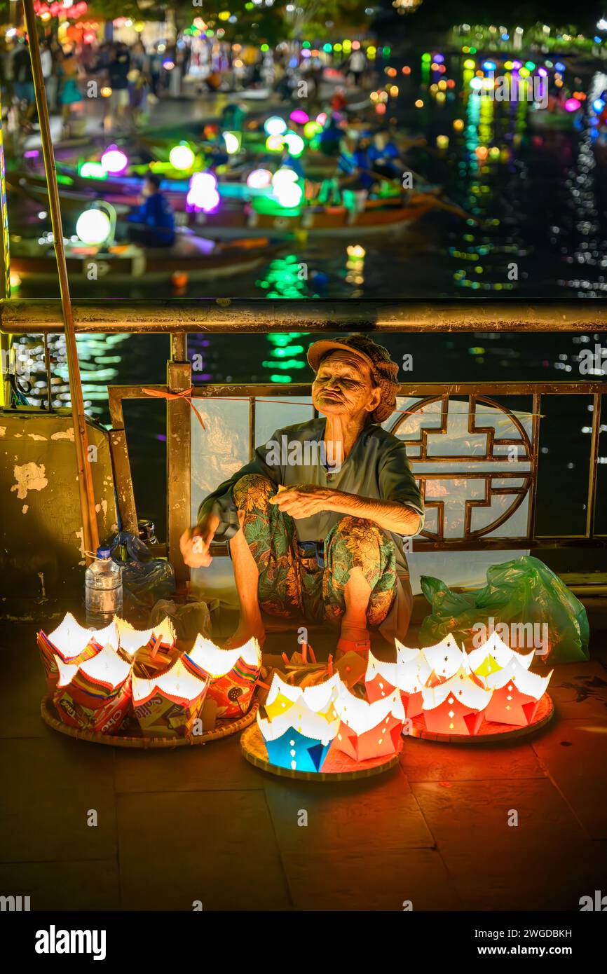 An Elderly Lady selling lanterns on the Golden Bridge at night, Hoi An, Vietnam Stock Photo