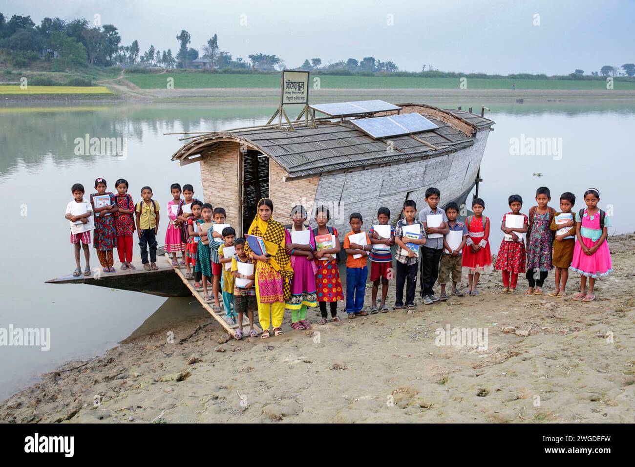 Students of class III, pose for a group photo after the end of the classes in front of the Horondarpur Boat School. The country had floods twice in 2007 and 332 schools destroyed and 4,893 schools were damaged. Shidhulai operates a fleet of floating schools, libraries, health clinics, solar workshops and floating training centres with wireless internet access, serving close to 97,000 families in flood-prone regions. Boats themselves are outfitted with solar panels that power computers, lights and medical equipment. Horondarpur, B L Bari Faridpur, Pabna, Bangladesh. Stock Photo