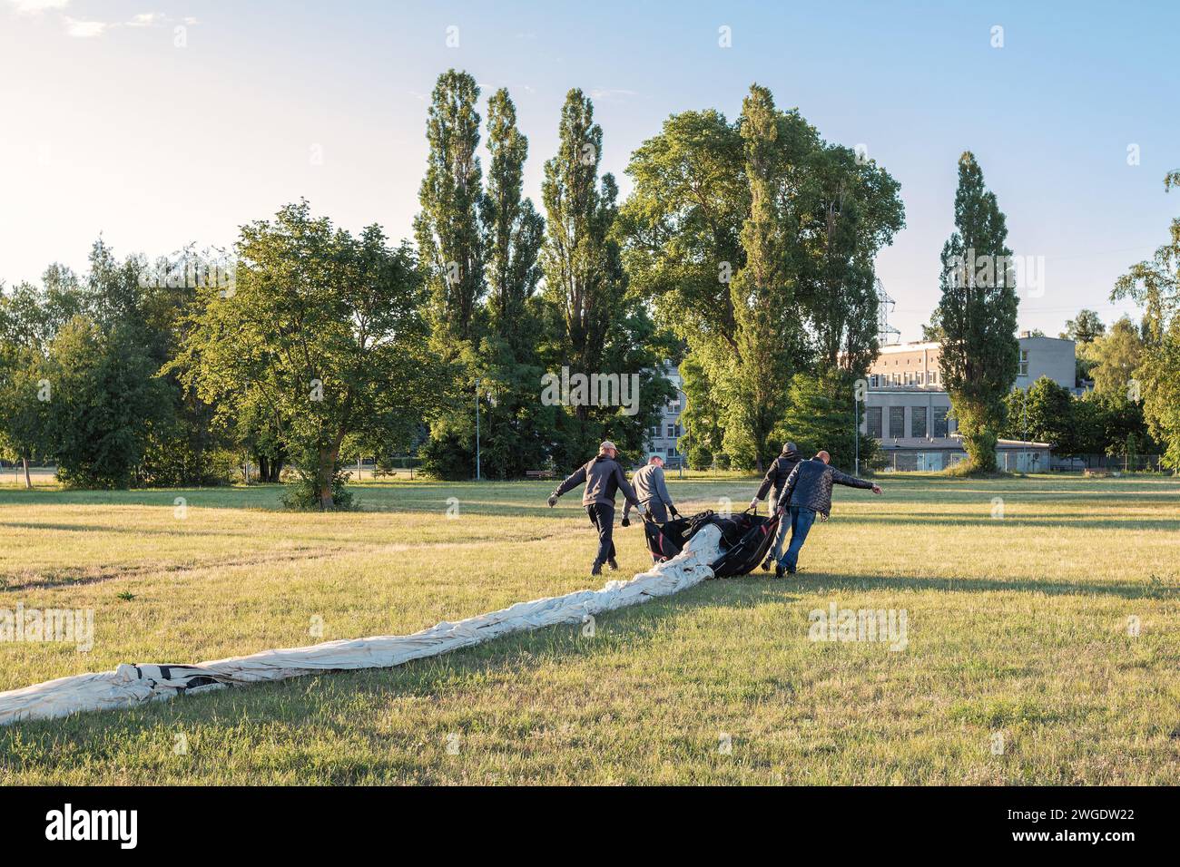 Four strong men unpack the fabric of a hot air balloon while stretching it out in a meadow. Stock Photo