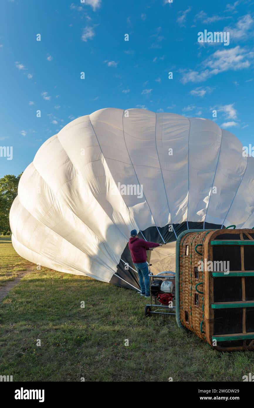 A man is holding a white hot air balloon lying on its side, cold air is being blown into the balloon to prepare it for the shield. Stock Photo