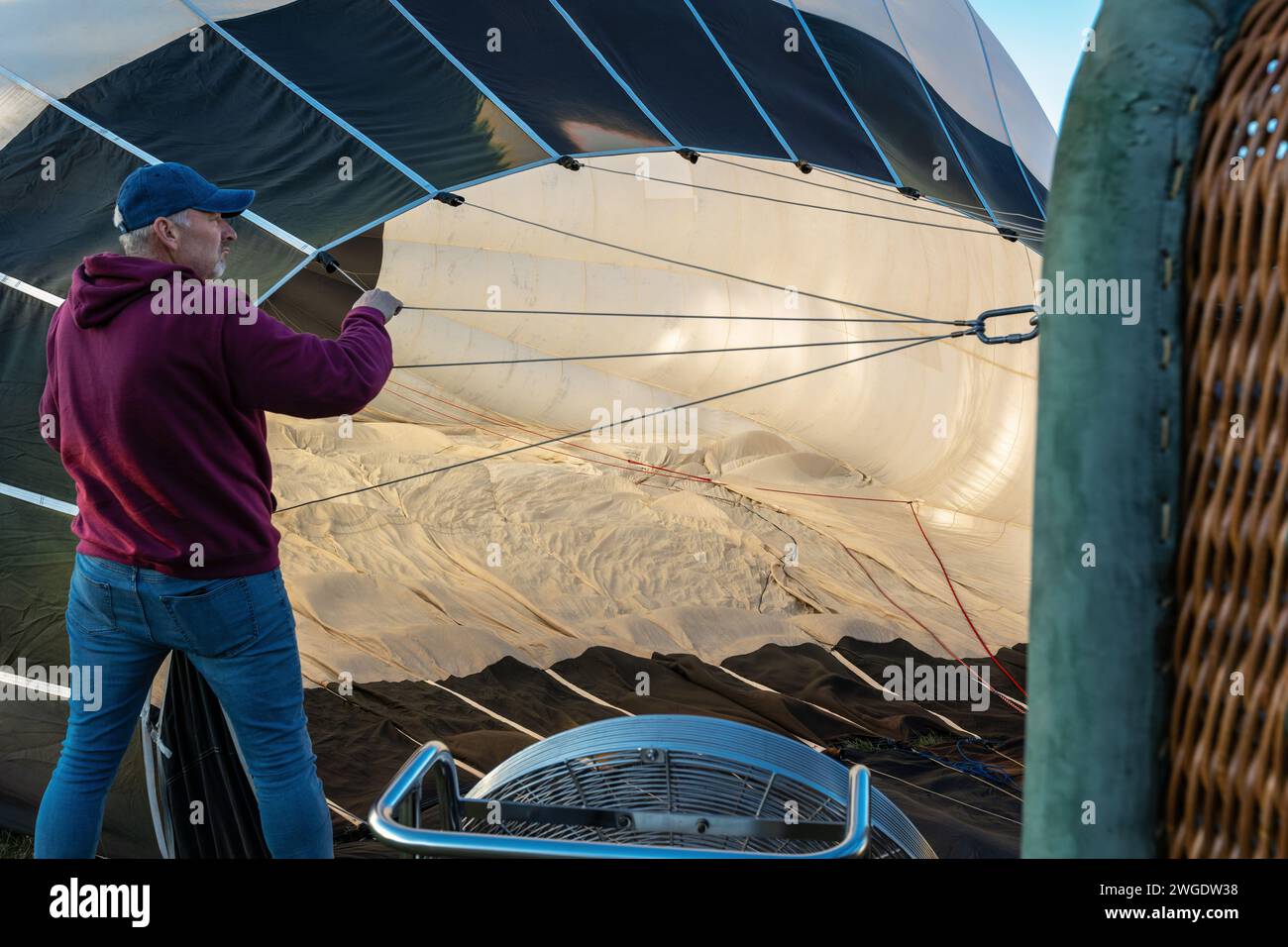 Men prepare a large hot air balloon for flight, one of them adjusts the folds of nylon material inside the balloon. Stock Photo