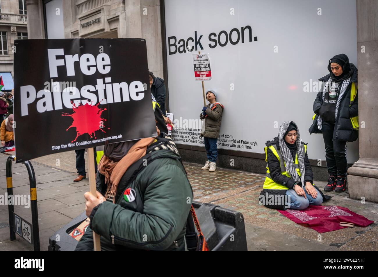 London, UK. 3rd February 2024. Free Palestine banner held by a peace activist / protester and a Muslim woman praying during the Pro - Palestine march near Oxford Street in Soho,  Free Palestine Movement, London, UK Stock Photo