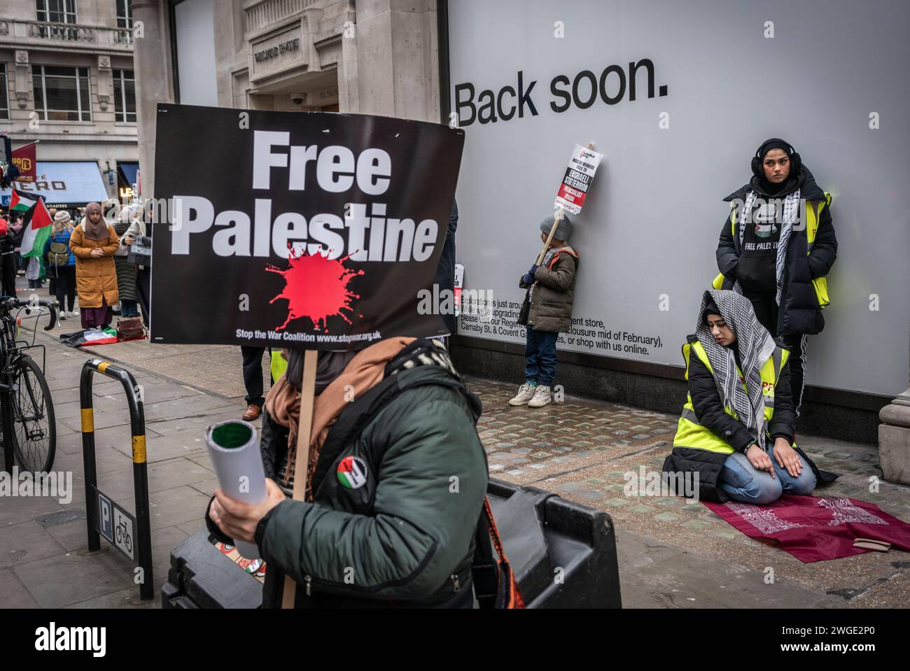 London, UK. 3rd February 2024. Free Palestine banner held by a peace activist / protester and a Muslim woman praying during the Pro - Palestine march near Oxford Street in Soho, Free Palestine Movement, London, UK Stock Photo