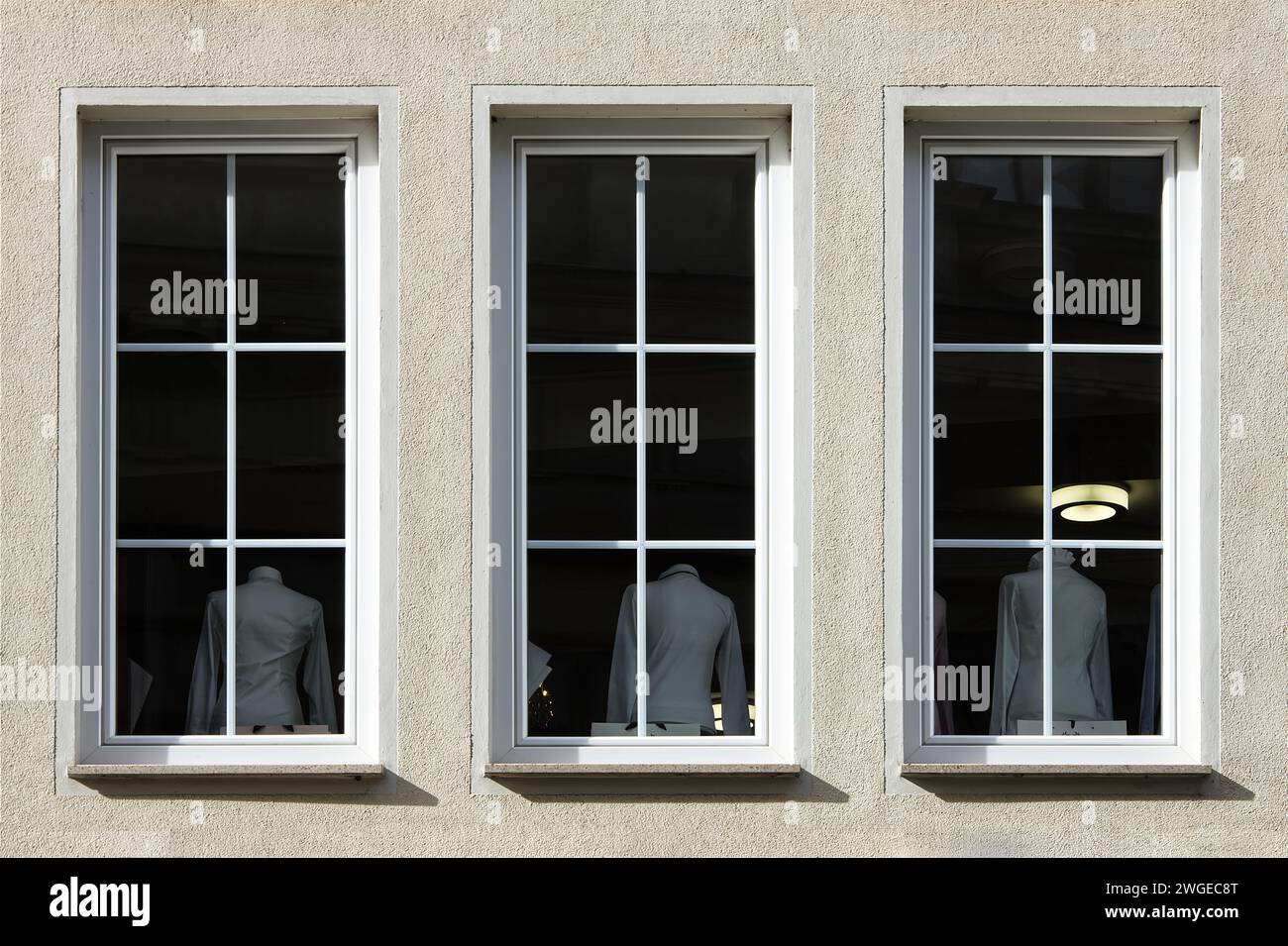 Part view of a facade with tree windows viewing three mannequins in white shirts Stock Photo
