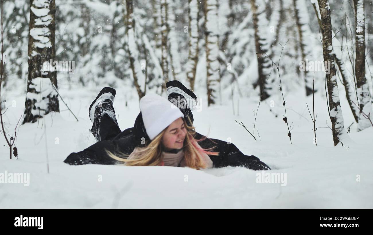 A girl falls on the snow in winter in the forest. Stock Photo