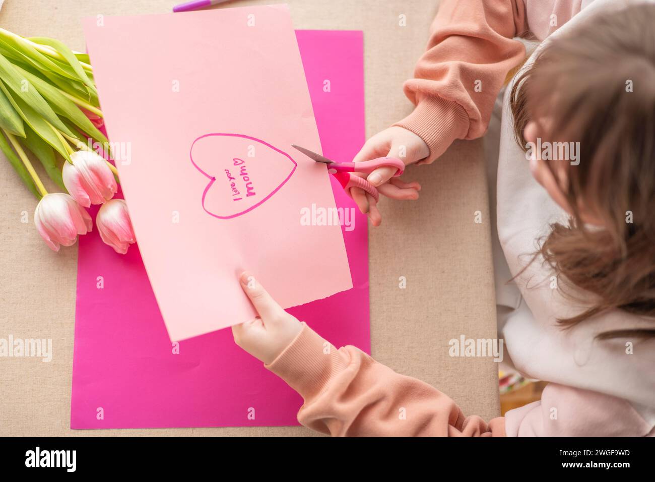 Mothers Day.moms day concept. DIY mom card.Child cuts a heart out of paper at the table. child makes a card for his mother.Flowers and cards for mom. Stock Photo