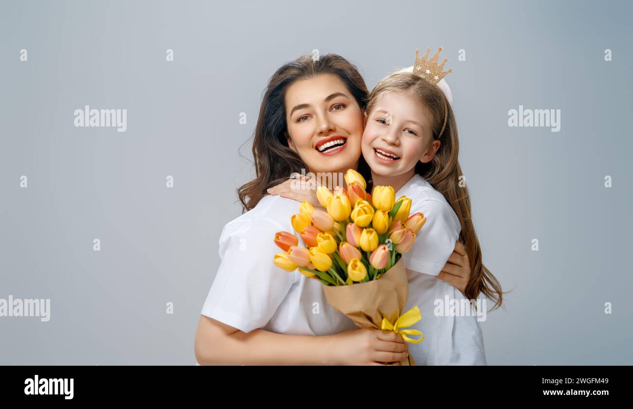 Happy women's day. Child is congratulating mom and giving her yellow flowers. Mum and girl smiling on light grey background. Family holiday and togeth Stock Photo