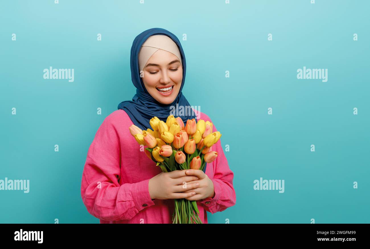 Beautiful young woman with yellow flowers in hands on teal wall background. Stock Photo