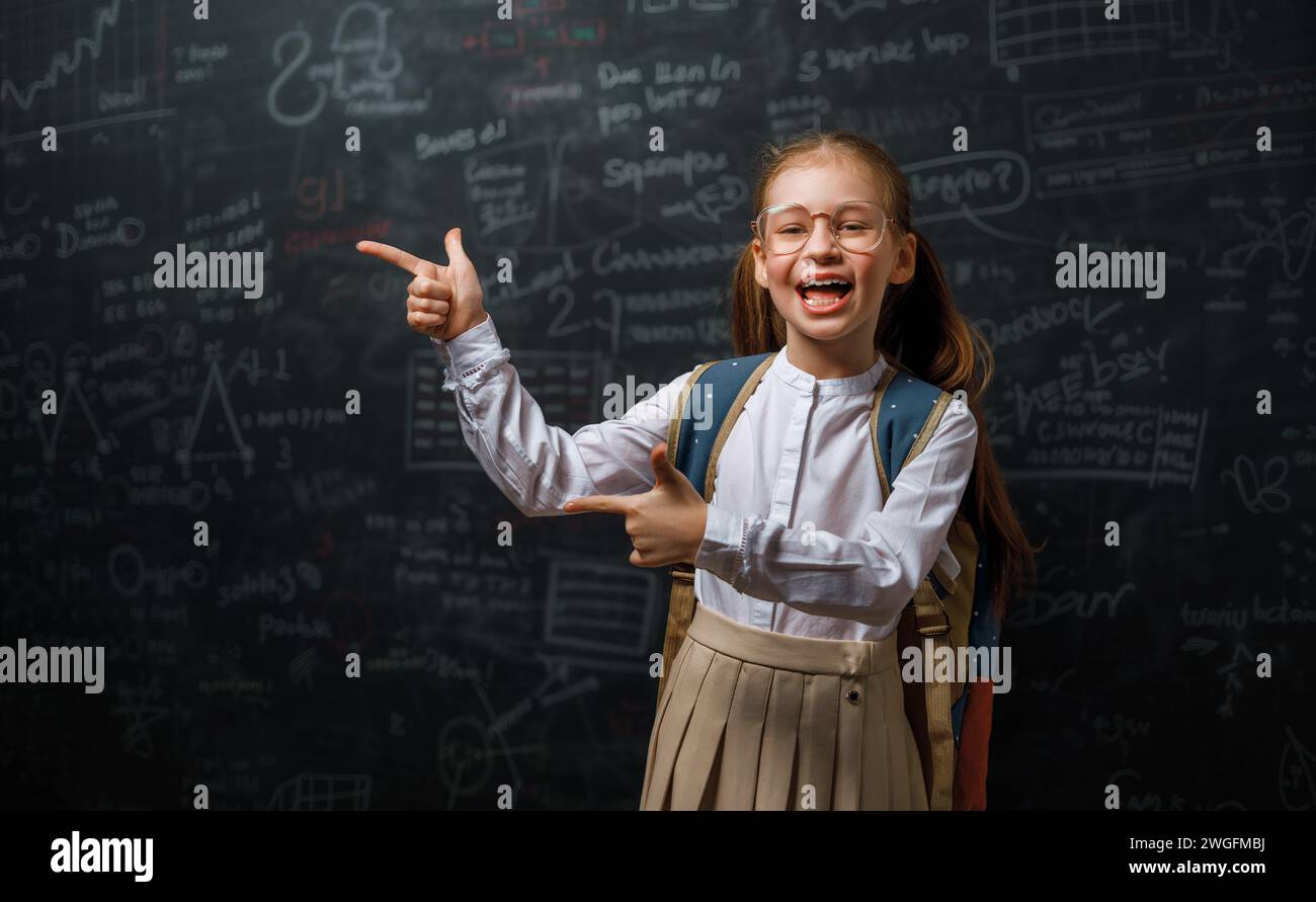 Back to school. Happy cute industrious child indoors. Kid is learning in class on background of blackboard. Stock Photo