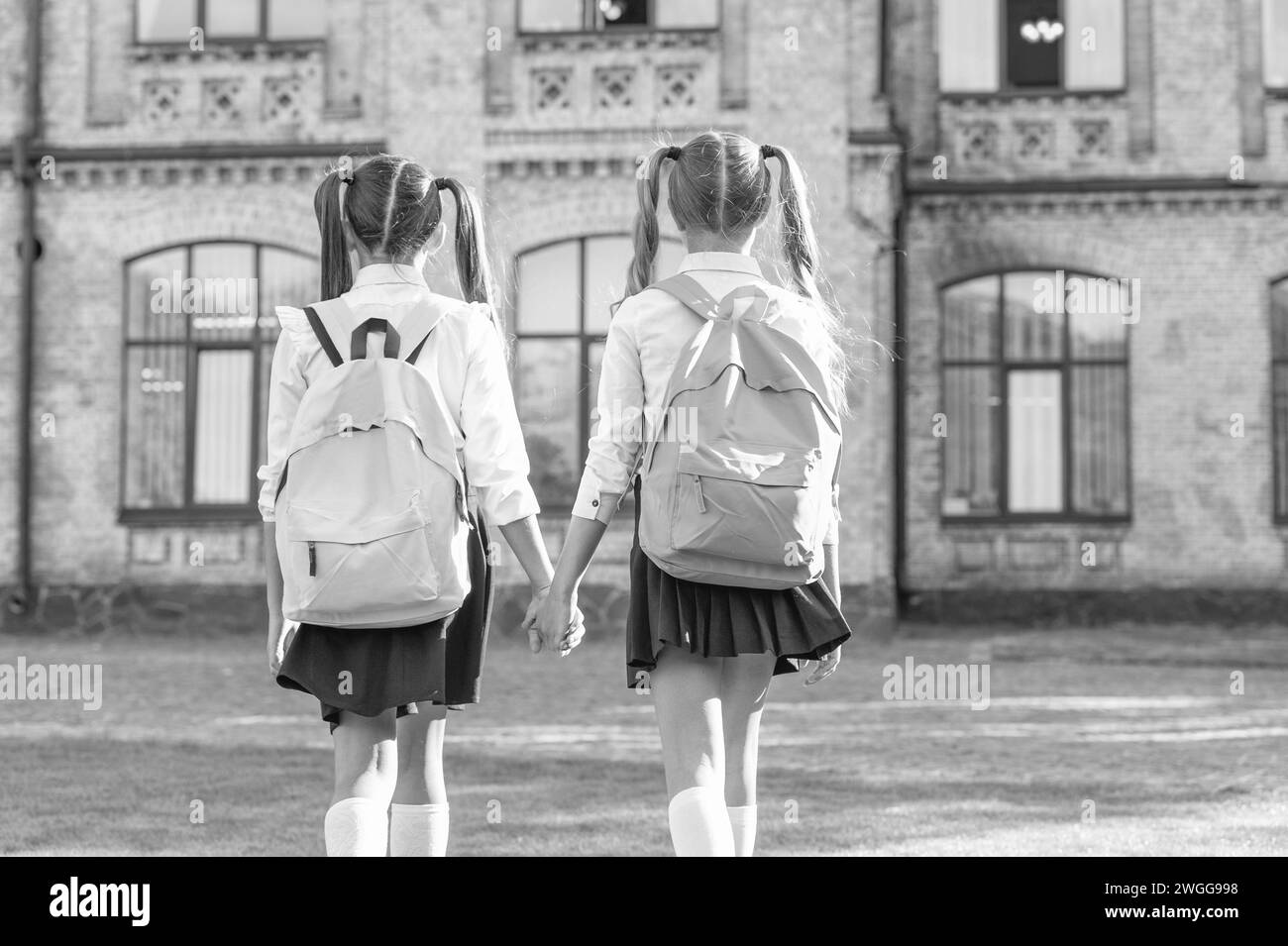 back view of two children with school backpack walking together outdoor ...