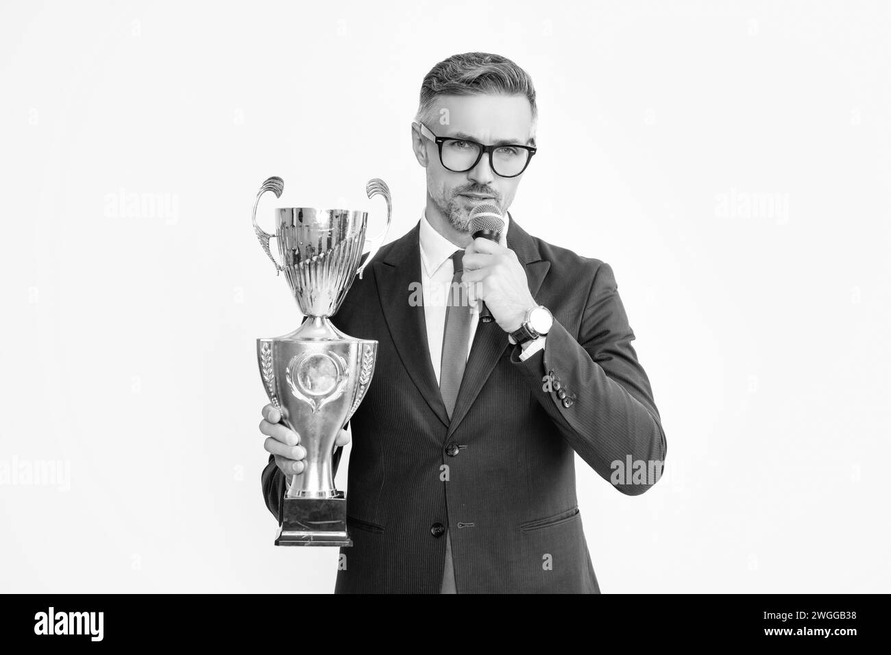 serious mature man in suit hold champion cup and microphone isolated on white background Stock Photo