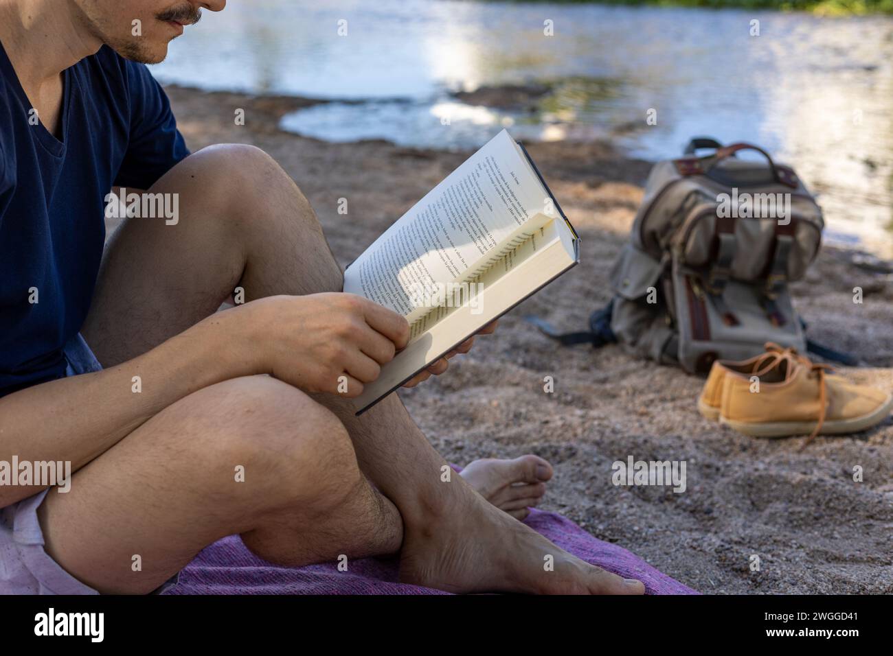 A man seated on the ground engrossed in reading a book placed on his lap. Stock Photo