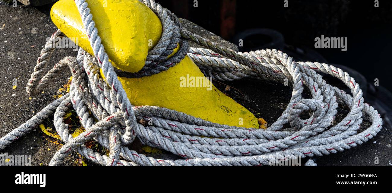 From above long single line rope tied to strong yellow bollard on dockside with concrete structure surface for facilitating mooring of boats at port Stock Photo
