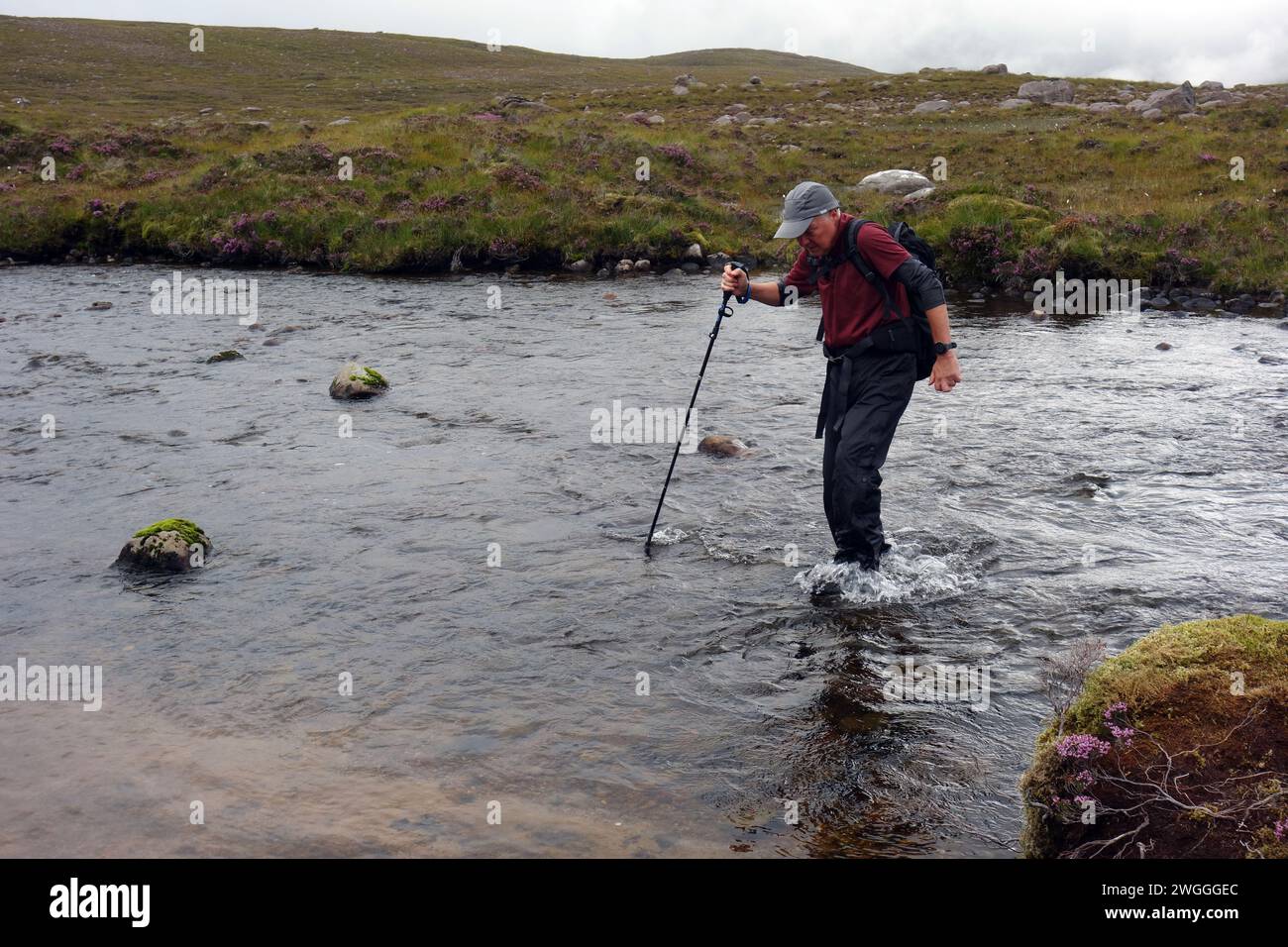 Man (Hiker) Wading River on the Outflow of 'Loch na h-Oidhche' in the Flowerdale Forest, Wester Ross, North West Highlands, Scotland, UK Stock Photo