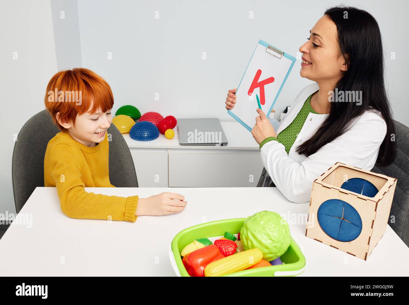 Red-haired boy during speech therapy session. Speech therapist teaching child to pronounce letter k Stock Photo
