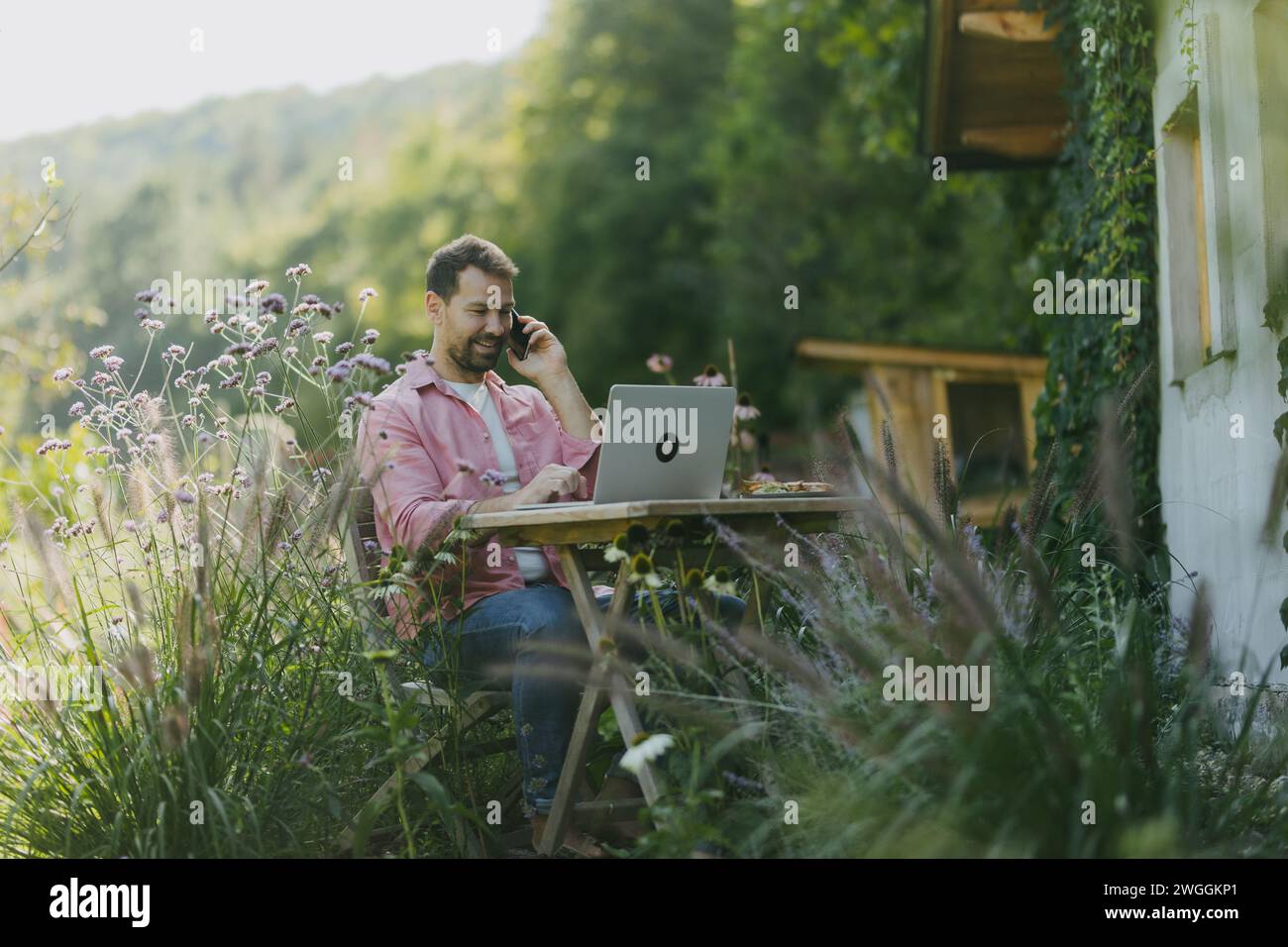 Man working in the garden on laptop, phone calling. Businessman working remotely from outdoor homeoffice, thinking about new business or creative idea Stock Photo