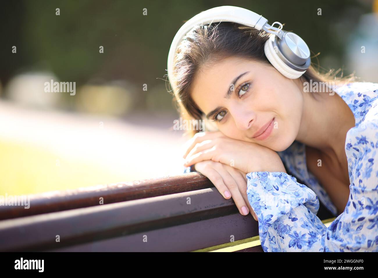 Relaxed woman looks at you listening audio with headphone in a park Stock Photo