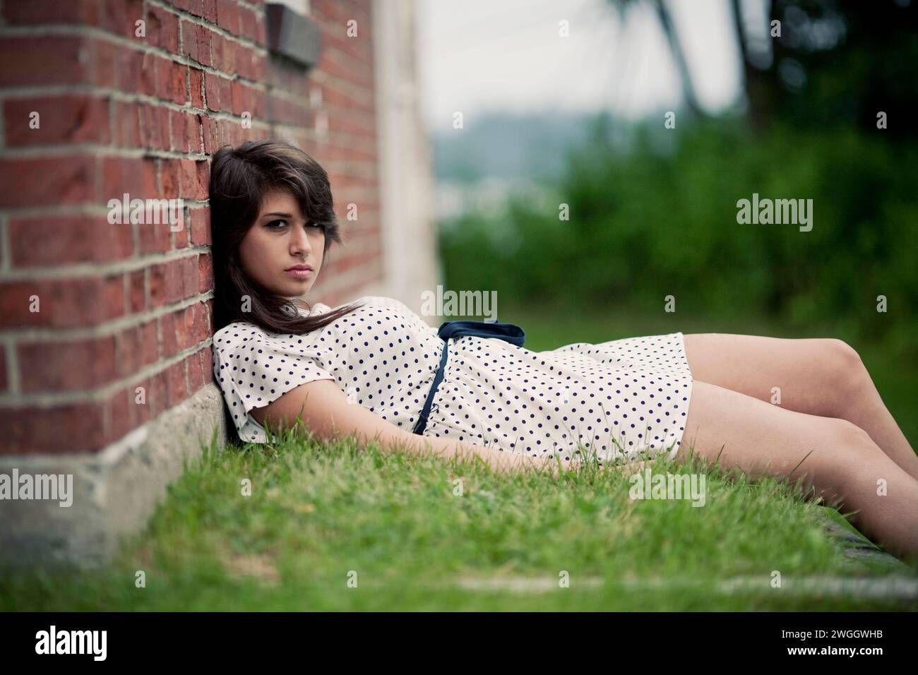 A teenager wearing a polka dot dress leans against a brick wall Stock ...