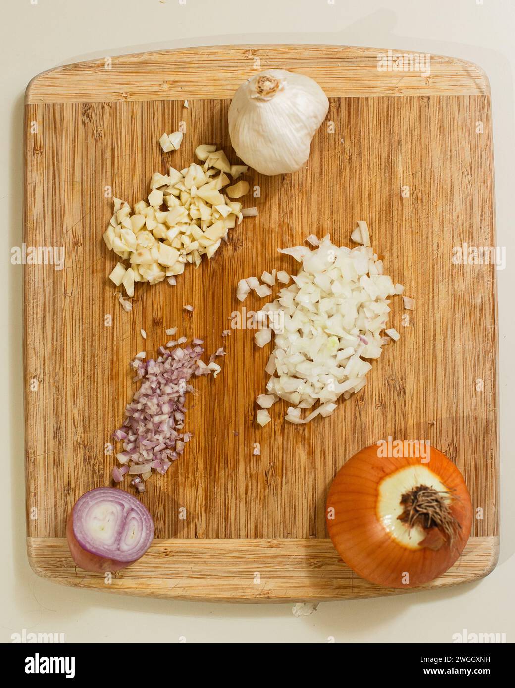 Wooden cutting board with onion, shallot and garlic bulb Stock Photo