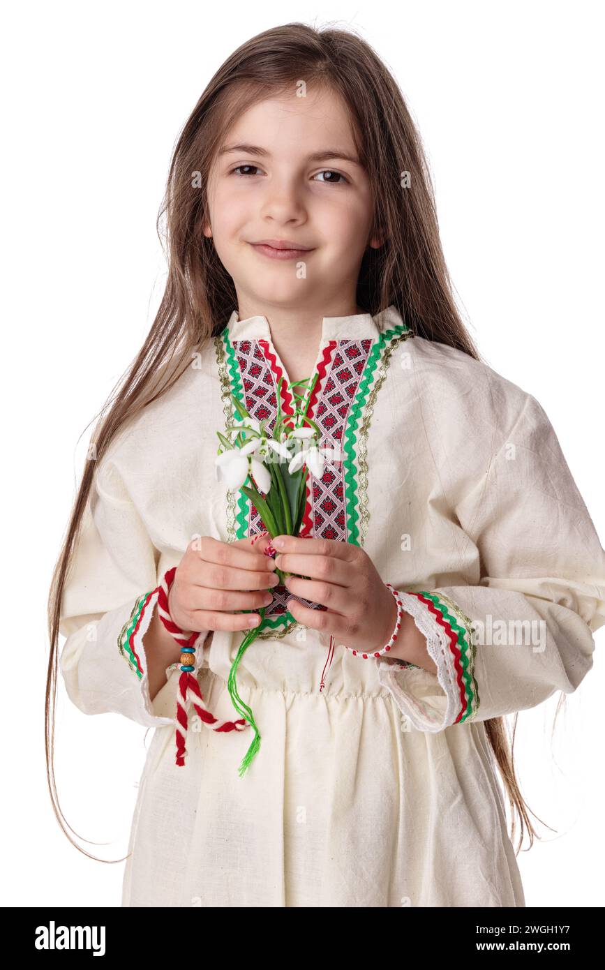 Bulgarian girl in traditional folklore costumes with spring flowers snowdrop and handcraft wool bracelet martenitsa symbol of Baba Marta Stock Photo