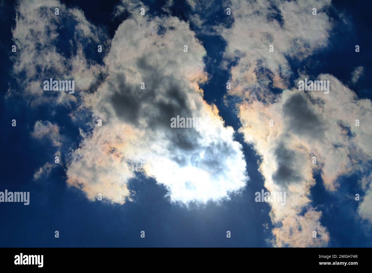 Looking straight up at a triangular cloud blocking the sun overhead, creating dramatic shadows and a bright silver lining Stock Photo