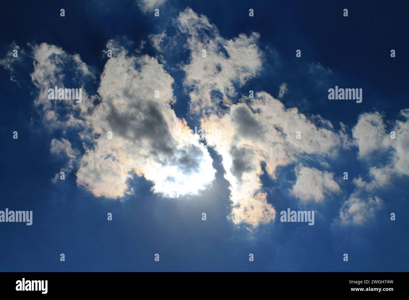 Looking straight up at a triangular cloud blocking the sun overhead, creating dramatic shadows and a bright silver lining Stock Photo