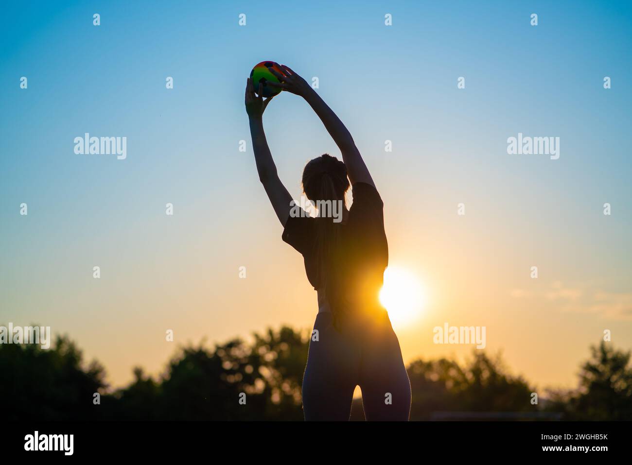 silhouette of a young woman doing gymnastics with a ball against the backdrop of the early rising sun One Person Silhouette Enjoying the Sunset on a B Stock Photo