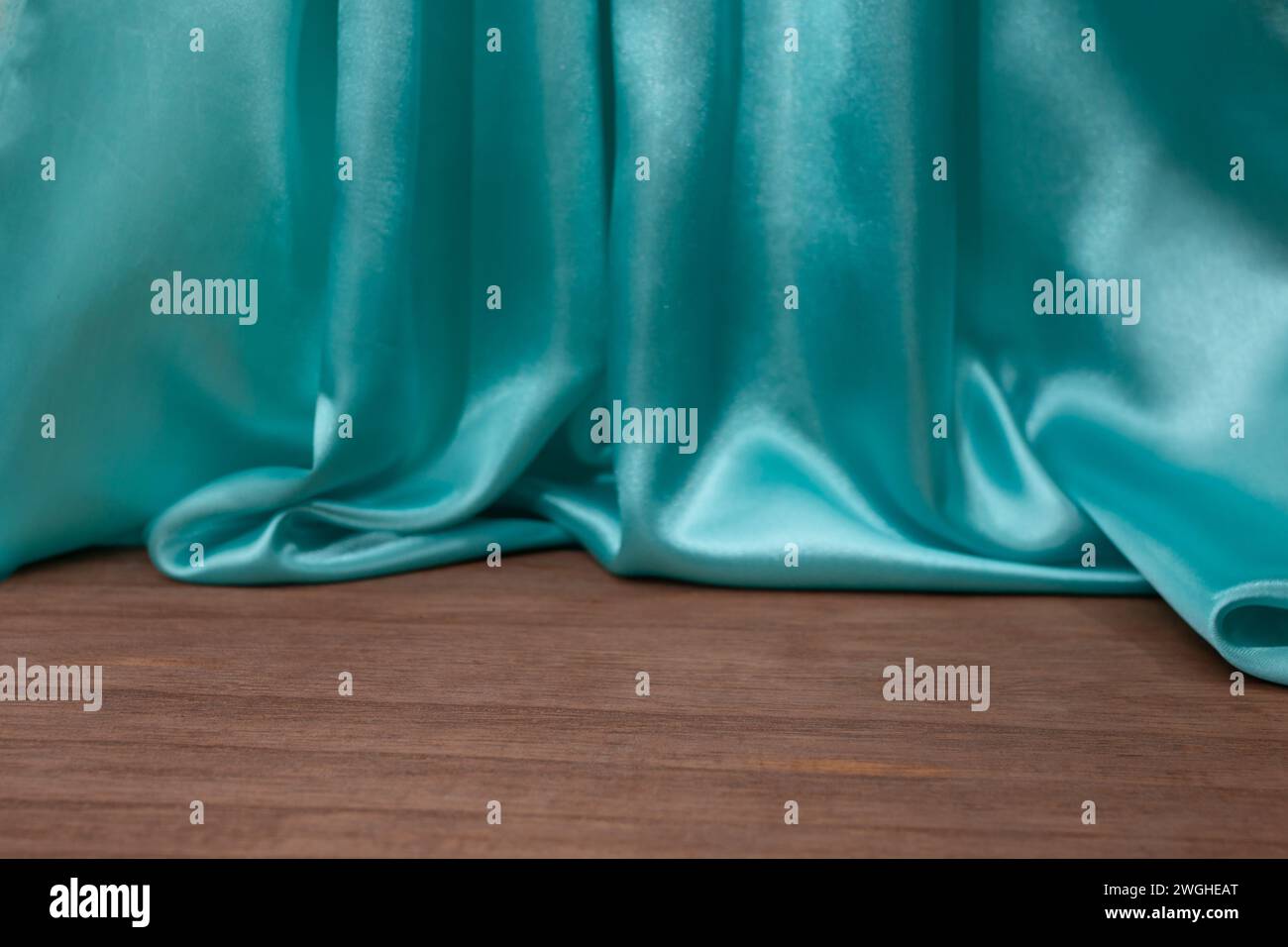 empty wooden floor with Elegant wavy turquoise satin cloth curtains, defocused in the background, product placement backdrop Stock Photo