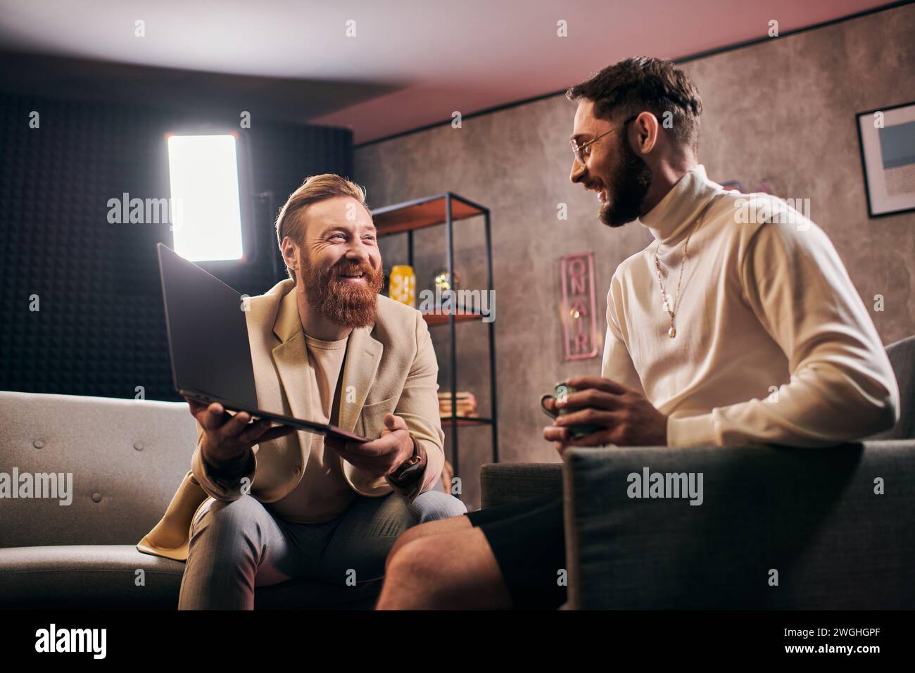 Man Studio Interview two joyous attractive men in elegant attires with coffee and laptop ...