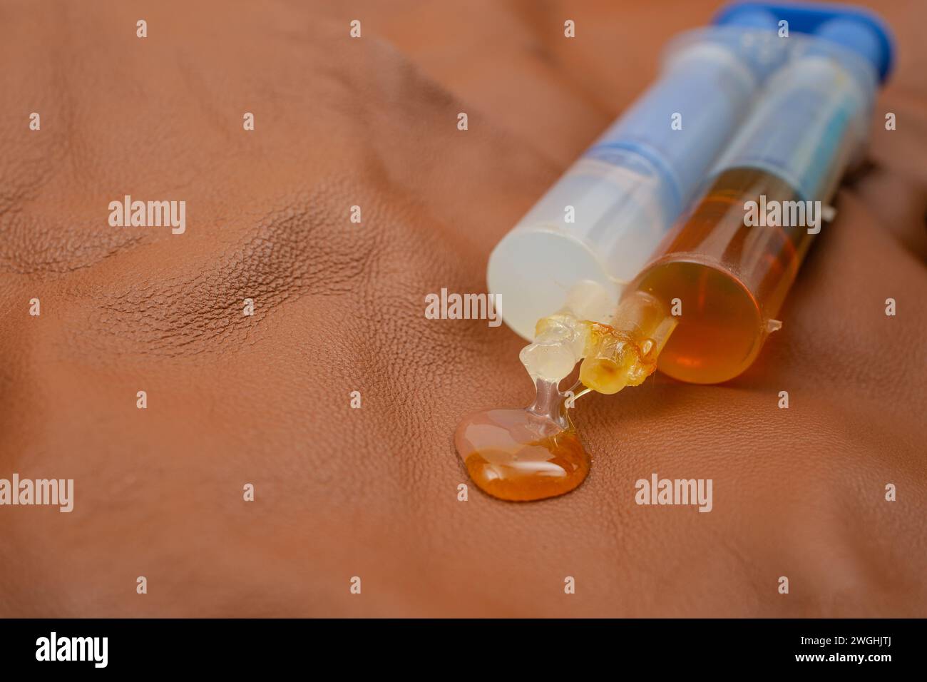 Double syringe with epoxy gel glue spilling on genuine brown leather