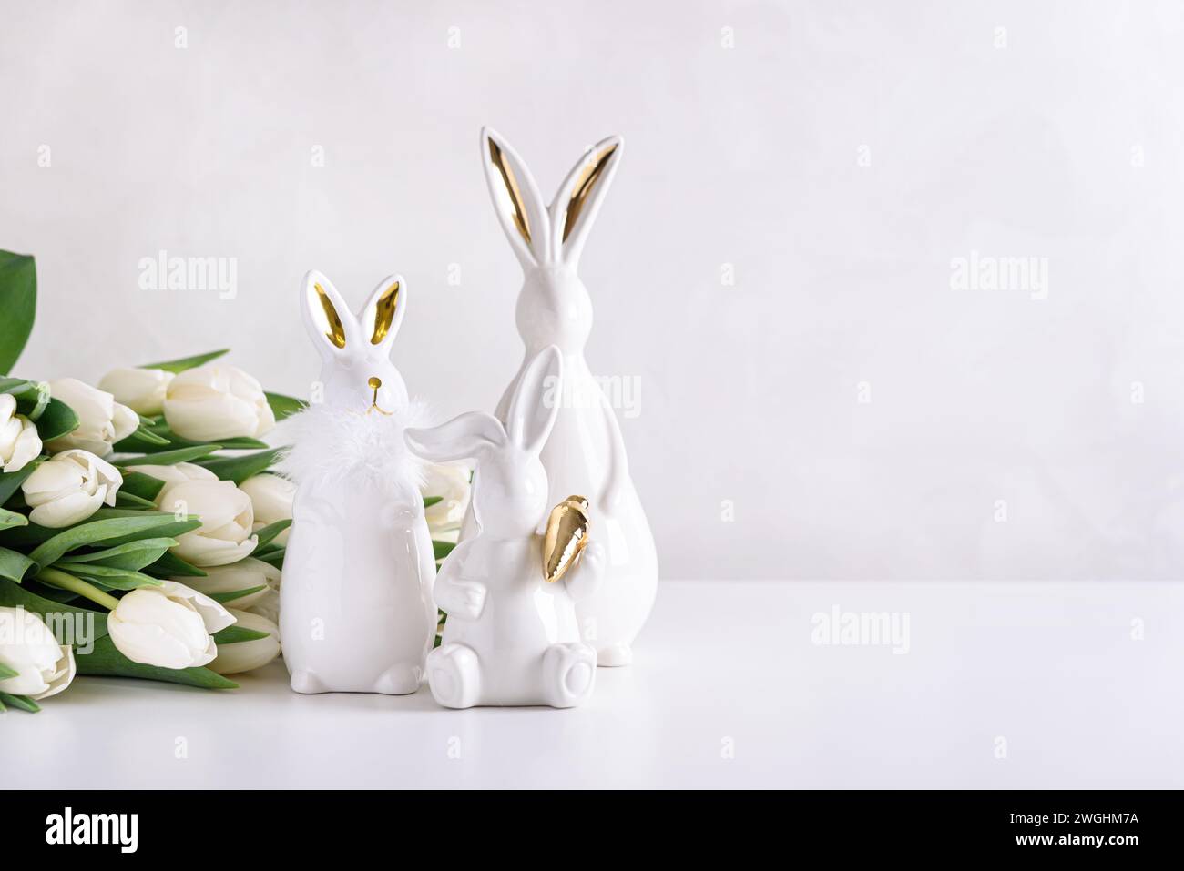 Three Easter rabbits figurines with bouquet of white tulips on white background. Easter celebration concept. Copy space. Front view Stock Photo